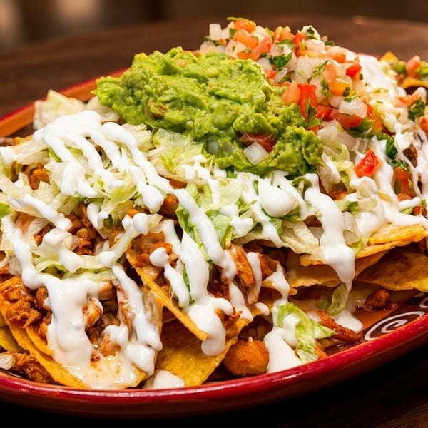 A vibrant plate of loaded nachos with chicken, guacamole, pico de gallo, and sour cream.