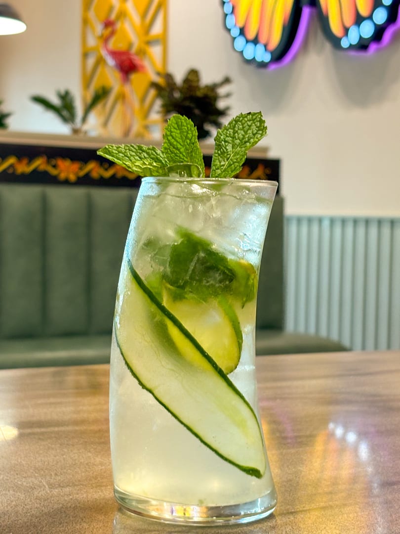 Refreshing cucumber and mint mojito in a tall glass on a wooden table with restaurant decor.