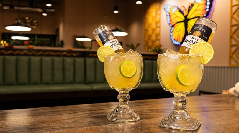 Two Corona-ritas with lime and salt on a wooden table in a restaurant with a butterfly decoration.