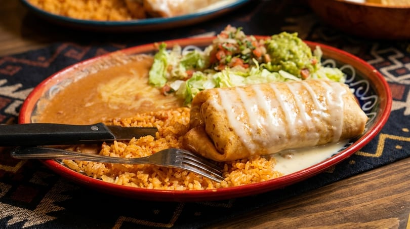 A large burrito covered in white sauce, with rice, refried beans, lettuce, pico de gallo, and guacamole.